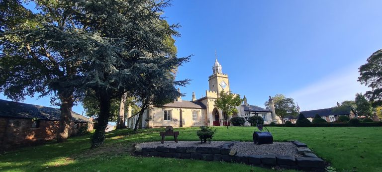 Historic building surrounded by greenery and trees under a clear blue sky.